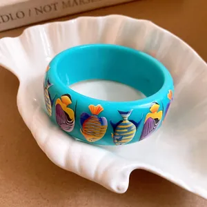 Turquoise resin wide bangle with colorful tropical fish prints on white shell dish