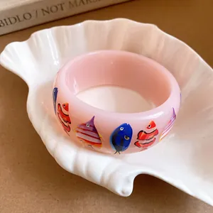 Macro detail of a wide pink resin bangle featuring colorful tropical fish prints for vacation style