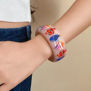 Close-up detail of a wide translucent resin bangle with colorful tropical fish prints