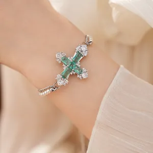 Detail of an elegant emerald green cross bracelet with cubic zirconia and pearl strands