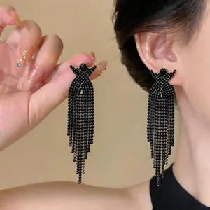 Dettaglio di eleganti orecchini a nappa con strass neri e design a croce a X indossati all'orecchio