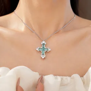 Detailed close-up of a silver cross necklace with emerald green zirconia on a model.
