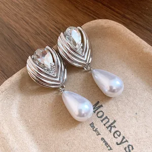 Dettaglio di orecchini a goccia in argento con cristalli e perle su un vassoio di carta beige.