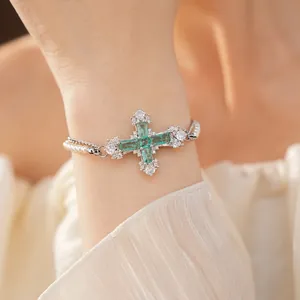 Close-up detail of an elegant emerald green cross bracelet with a pearl chain on wrist