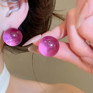 Detailed close-up of translucent purple resin ball earrings shown on ear and hand