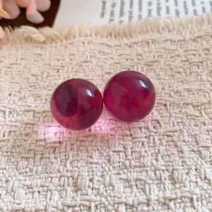 Close-up of translucent dark red resin ball stud earrings on a textured fabric background.