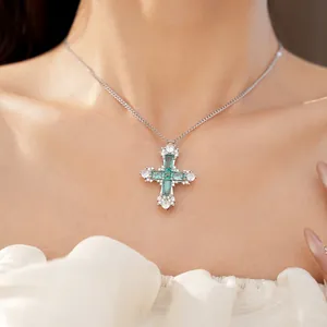 Detailed view of silver cross necklace featuring emerald green and clear cubic zirconia
