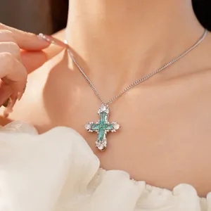 Close-up of elegant silver necklace with green zircon cross pendant worn on neck