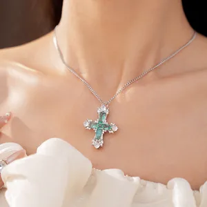 Elegant silver cross necklace with emerald green and clear zircon stones worn by model