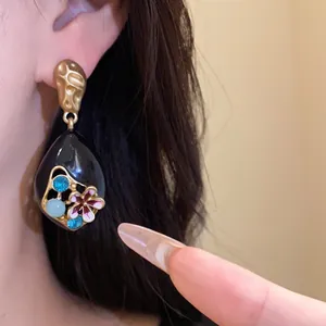 Dettaglio di orecchini vintage neri con fiori in smalto e cristalli blu lucenti