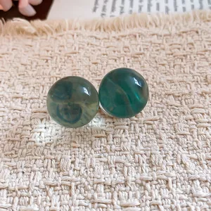 Close-up of translucent green resin ball stud earrings on textured fabric background