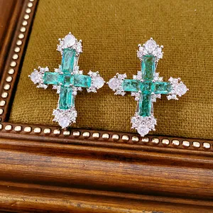 Detailed macro of emerald green zircon cross earrings on a vintage velvet display tray