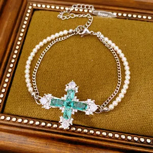 Detail view of cross pendant necklace with green crystals and faux pearls on velvet.