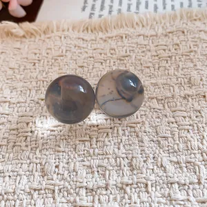 Detail of translucent grey resin ball stud earrings on textured cream fabric
