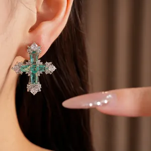 Close-up of elegant cross earring with green and white zircon stones.
