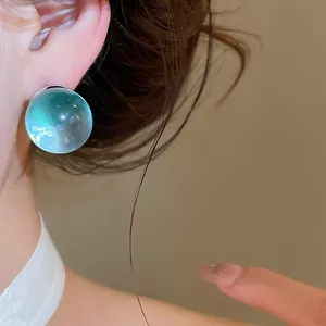 Close-up view of an icy transparent light green resin ball stud earring worn on ear
