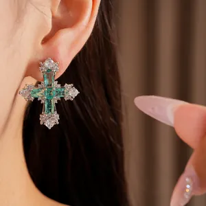 Macro detail of luxury silver cross earring featuring emerald green and clear zircons.