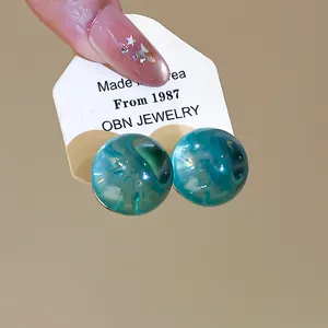 Close-up of translucent teal resin ball earrings with silver needles on display card