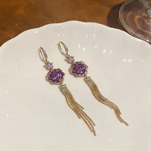 Detailed macro shot of elegant purple rose earrings with long gold tassel chains on a white plate