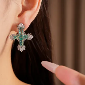 Close-up of a sparkling silver cross earring with green and white cubic zirconia