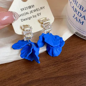 Detalle exquisito de pendientes de pétalos azul Klein con brillantes circonitas rectangulares
