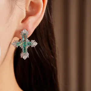 Elegant cross earring detail with green and clear zircons shown on an Asian model's ear