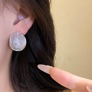 Detail showing a silver mesh hollow oval stud earring with shimmering stones on an ear.