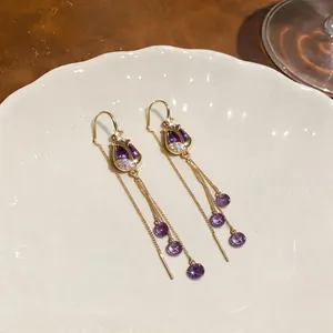 Detail view of 18k gold plated tulip earrings with purple zircon and tassel chains