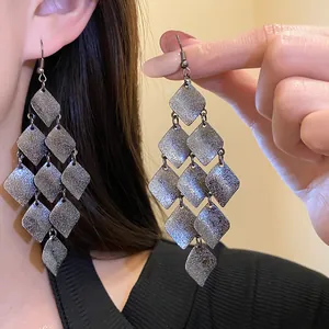 Detailed close-up showing matte grey rhombus tassel earrings worn by a female model
