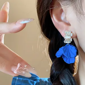 Primer plano de pendientes de pétalos de acrílico azul Klein con cristales de circón