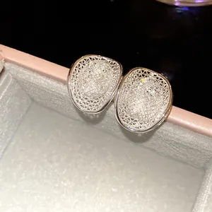 Close-up of hollow woven silver stud earrings with glittering pavé stones in a box.