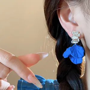 Primer plano de pendientes de pétalos acrílicos azul Klein con circonitas en la oreja de una modelo.