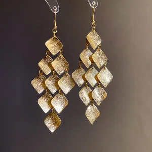 Detailed close-up of golden matte diamond-shaped tassel earrings with shimmering texture