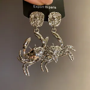 Detailed close-up of silver metal crab-shaped pendant earrings on a black display card.