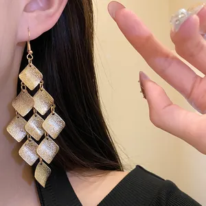 Detailed view of vintage matte gold rhombus tassel earrings worn by a model.