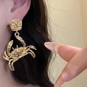Close-up detail of stylish gold-colored crab-shaped drop earrings worn on an ear