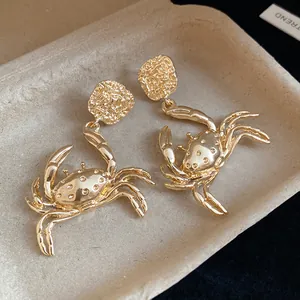 Detailed macro view of golden metallic crab drop earrings with textured square studs