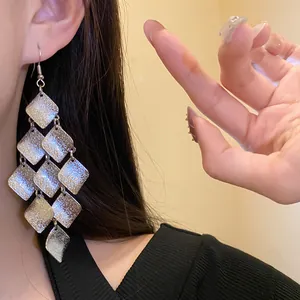 Detailed view of elegant matte silver rhombus tassel earrings worn by a model in a lifestyle setting