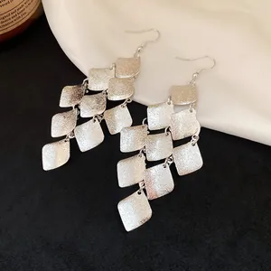 Detailed view of silver matte rhombus-shaped tassel earrings on contrast background