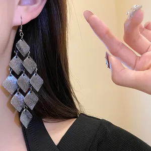 Close-up of matte grey diamond-shaped tassel dangle earrings worn by a model