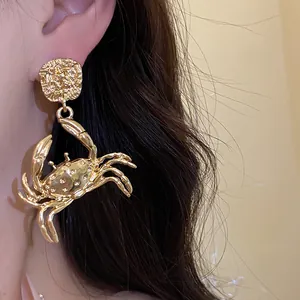 Detailed close-up of a gold metal crab pendant earring with intricate design textures.