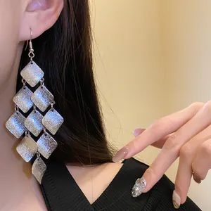 Macro detail of elegant matte silver rhombus fringe drop earrings worn by a model
