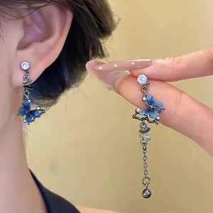 Gros plan de boucles d'oreilles papillon asymétriques avec résine bleue et zircons.