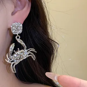 Detailed close-up shot of a silver-toned metal crab pendant earring on a model's ear