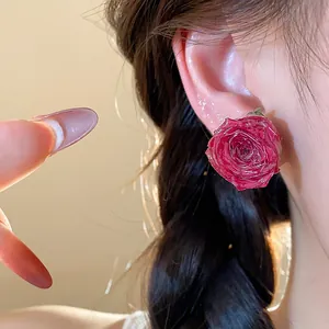 Close-up detail showing the delicate texture of a real red rose stud earring worn on ear.