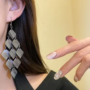Close-up of matte silver metal rhombus tassel earrings worn by a model