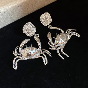 Detailed view of silver crab pendant earrings with textured metallic finish