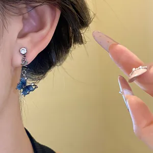 Détail d'une boucle d'oreille pendante papillon en résine bleue avec zircone