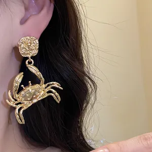 Detail view of a gold-colored metal crab pendant earring with a textured round stud