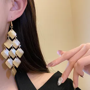 Close-up view of elegant matte gold rhombus tassel drop earrings worn by a model